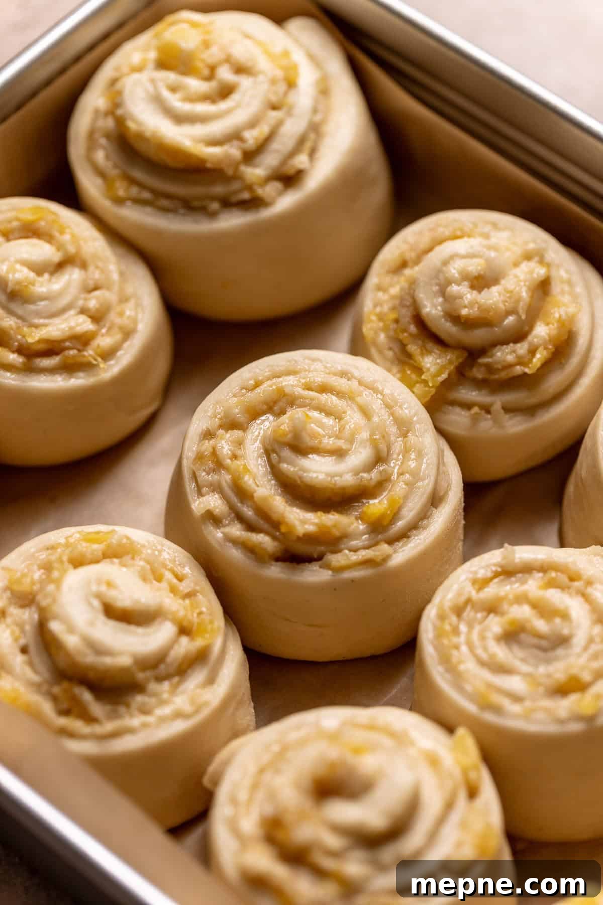 Tropical Pina Colada Cinnamon Rolls with Coconut Rum Icing 9 Pineapple coconut rolls in a baking pan barely touching before baking.