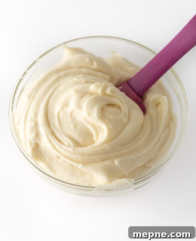 Cream Cheese Frosting Recipe for Cinnamon Rolls 3 Overhead view of fluffy cream cheese frosting in a glass bowl being stirred with a purple spatula