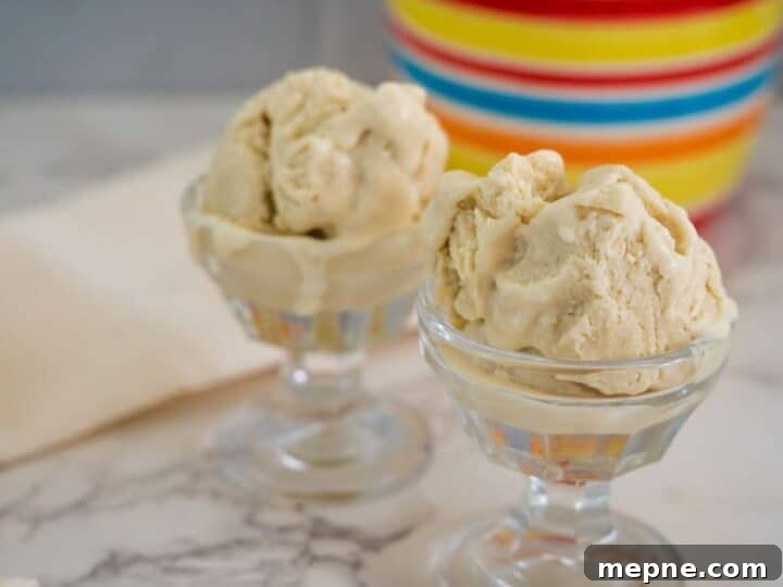 25 Low Carb Ice Cream Recipes for Creamy Keto Desserts 6 Two glass dessert bowls filled with scoops of beige-colored ice cream sit on a marble countertop, with a colorful striped container in the background.