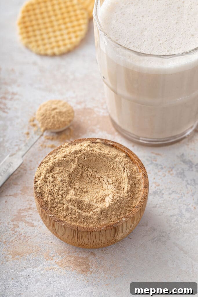 Small wooden bowl with maca powder next to a glass of maca latte