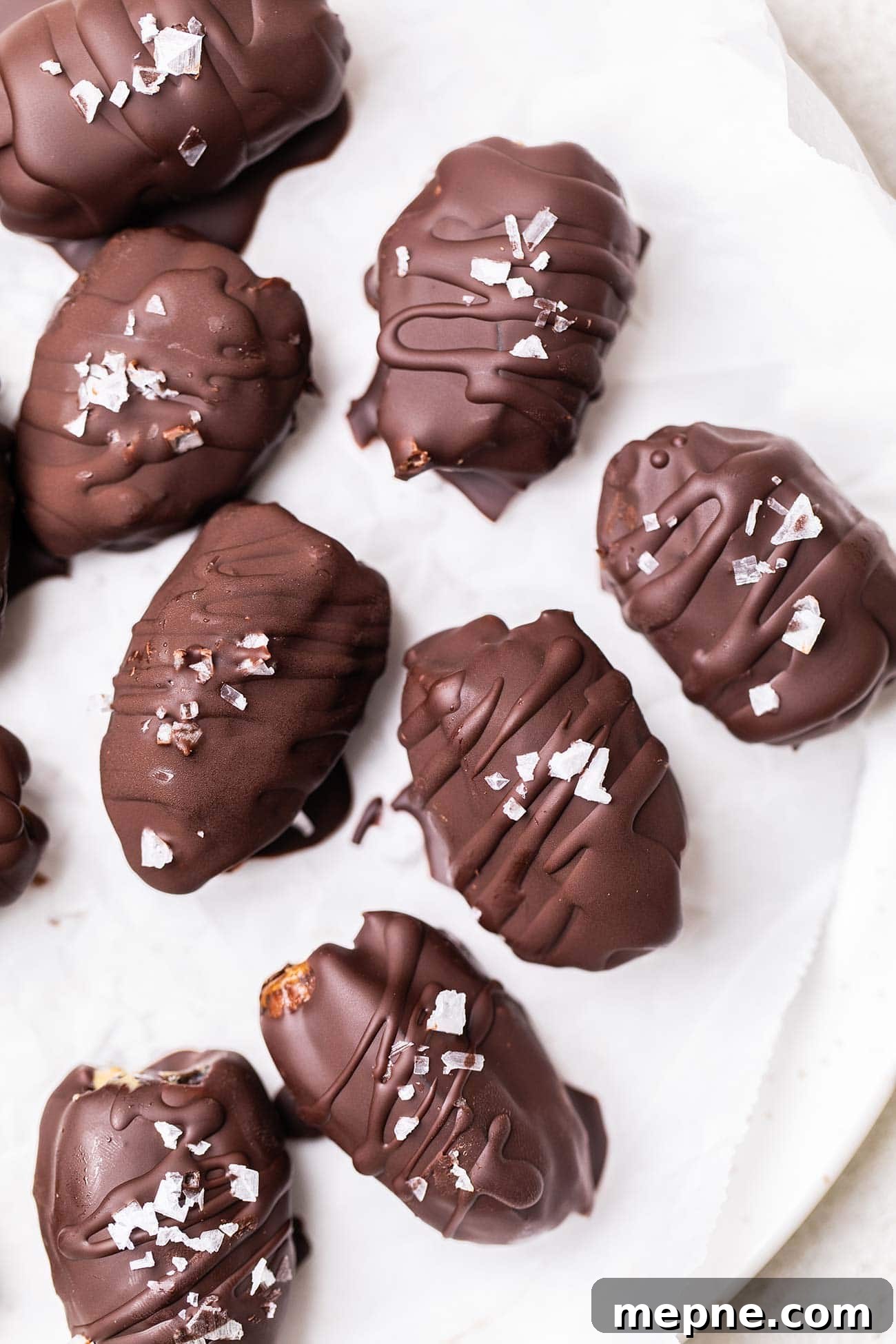 Chocolate-Stuffed Medjool Dates with Nut Butter 2 A white plate with dark chocolate covered dates sprinkled with flaky salt.