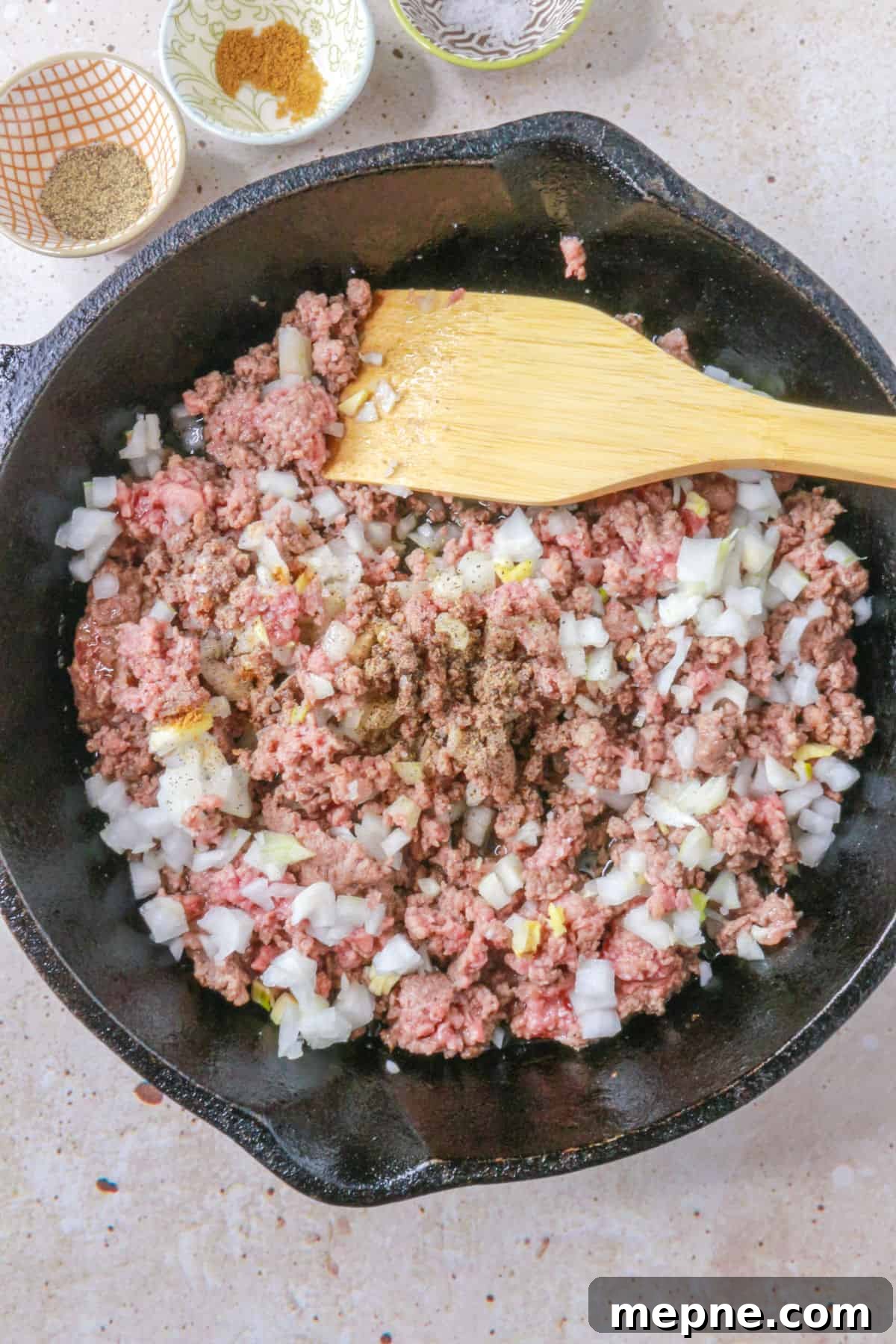 Ground beef, diced onion and garlic and spices in a cast-iron skillet