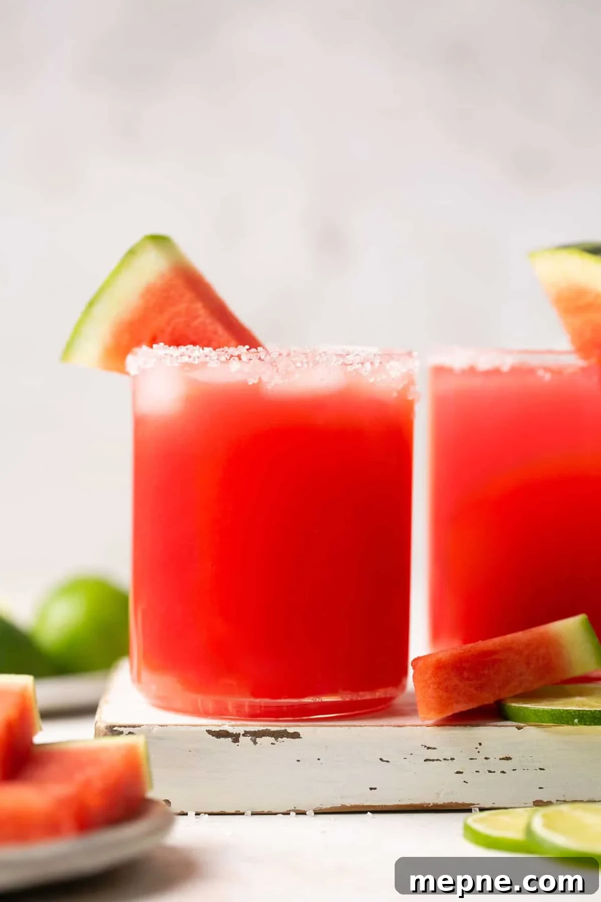 1800 Tequila Watermelon Margarita Recipe 2 a watermelon margarita in a salt-rimmed glass on a white board with a slice of watermelon for garnish