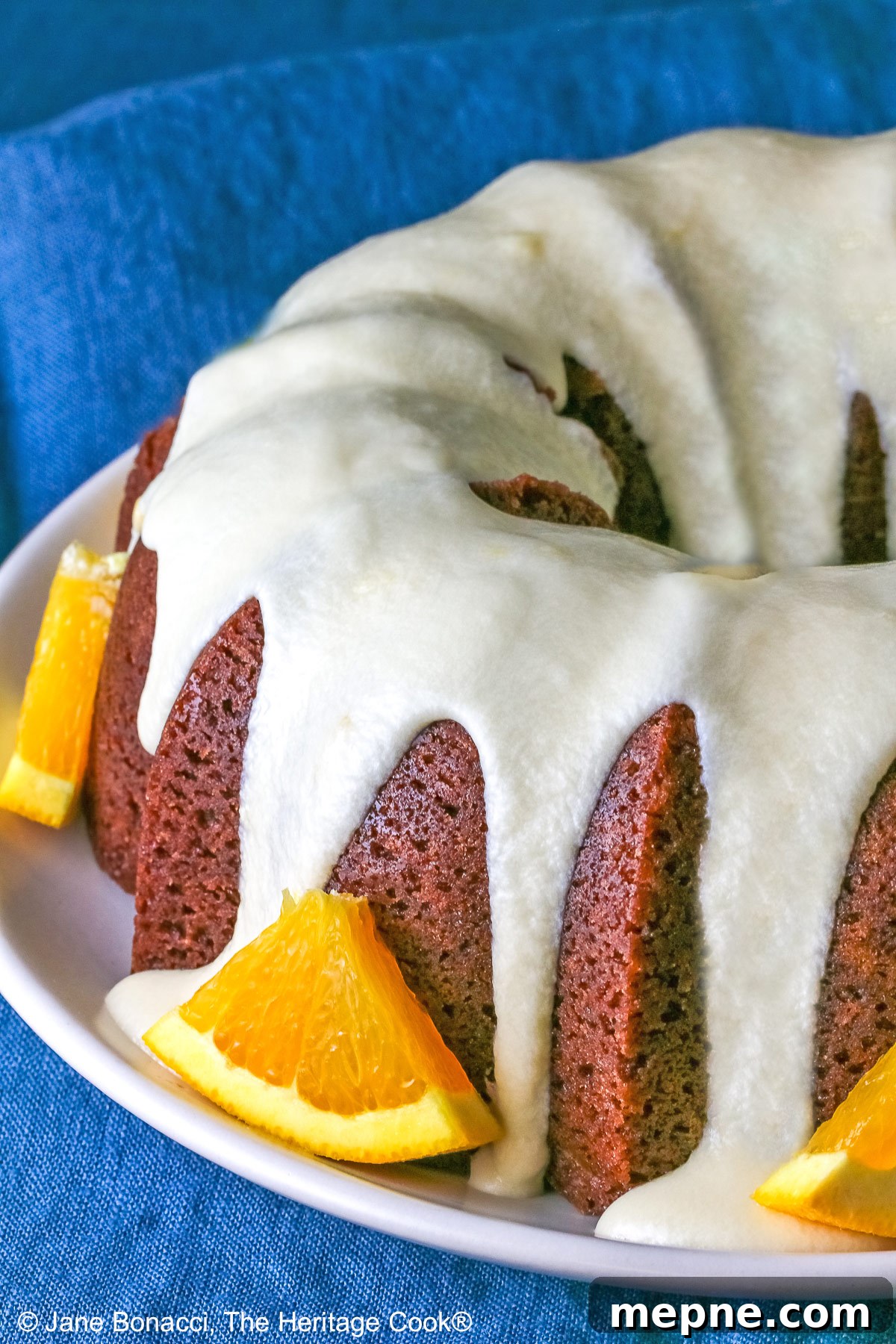 Gluten-Free Orange Chocolate Buttermilk Bundt Cake 4 Whole chocolate/orange bundt cake with cascading orange flavored glaze and fresh orange slices around the exterior on a white plate.