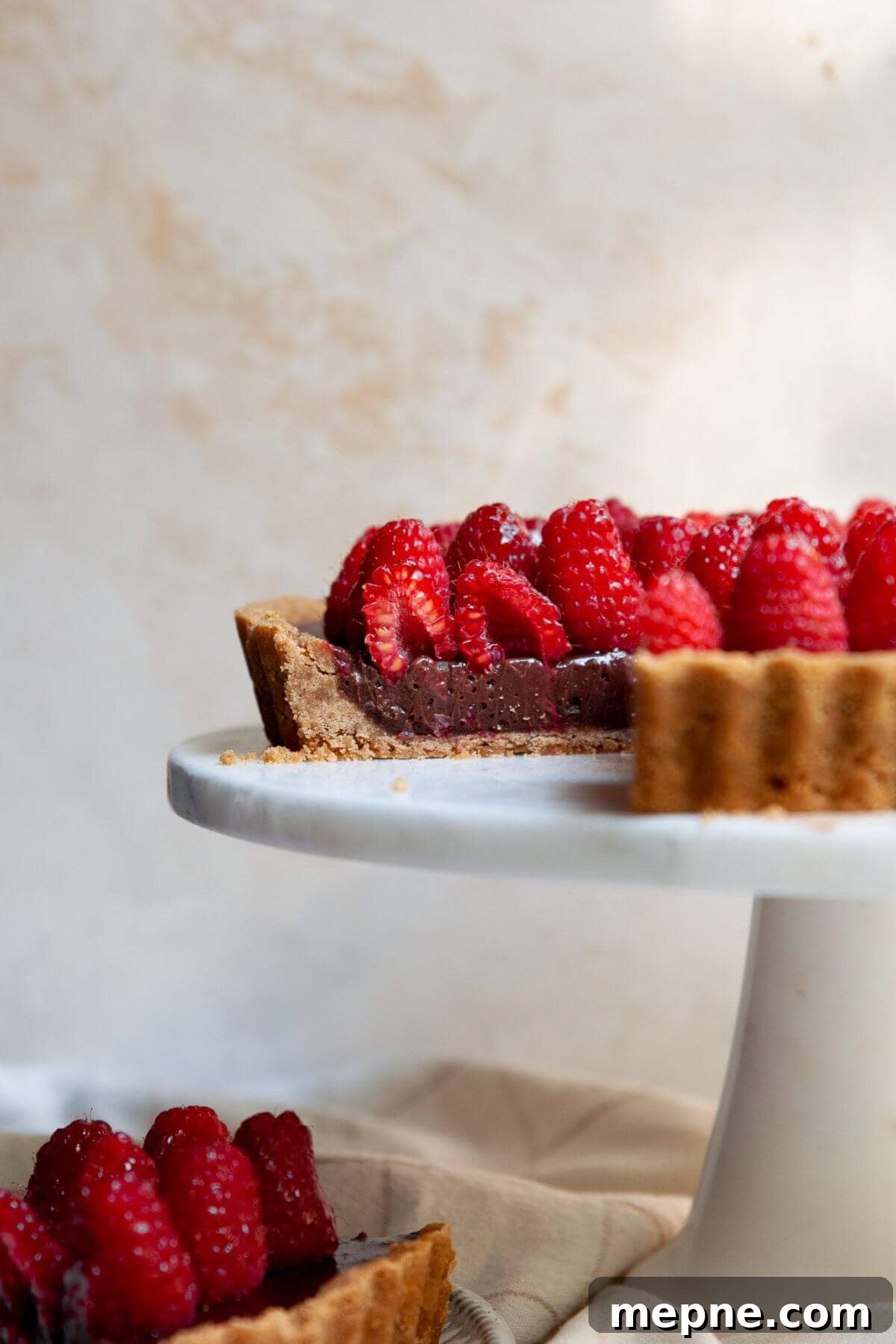 Dark Chocolate Raspberry Tart Recipe 2 Dark chocolate raspberry tart on a white cake stand, topped with fresh raspberries and a glossy honey-jam glaze.