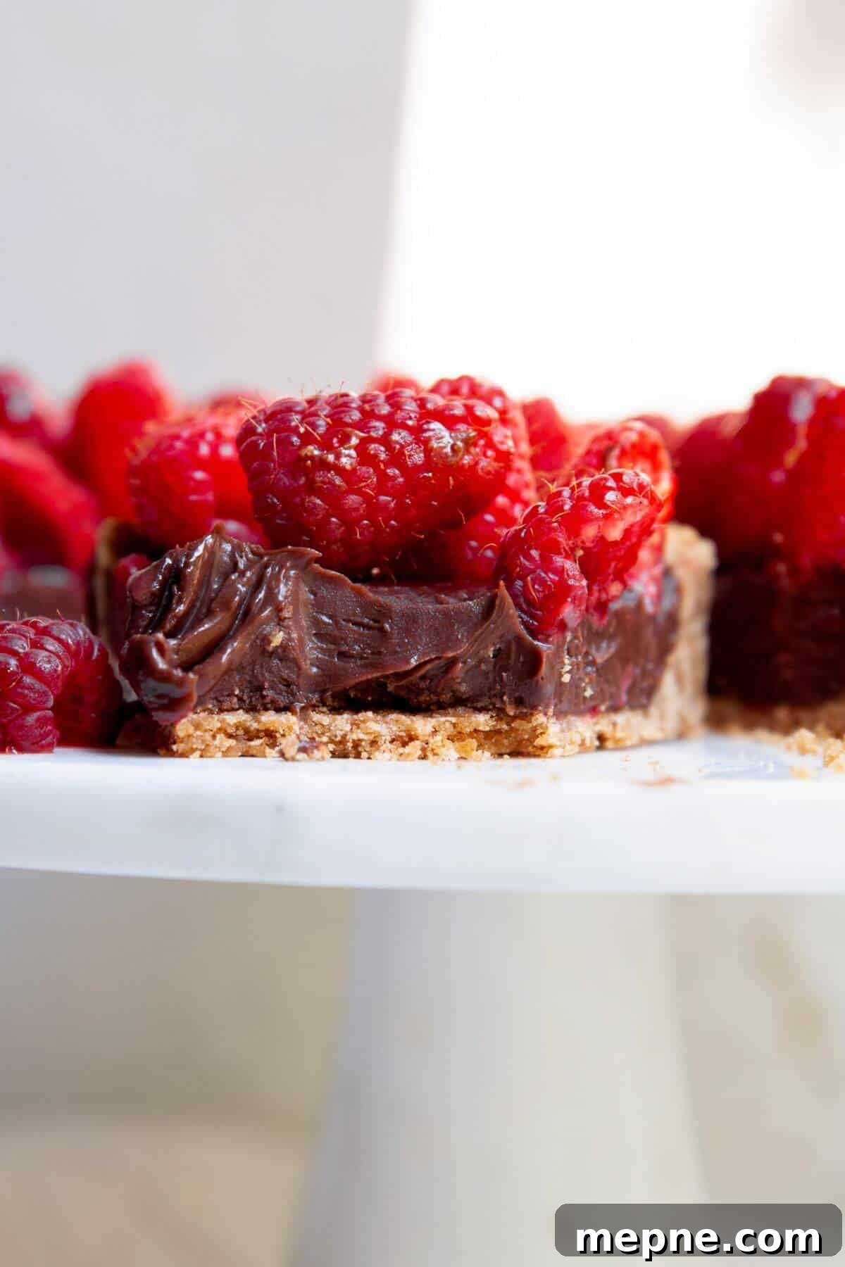 Dark Chocolate Raspberry Tart Recipe 11 Slice of dark chocolate raspberry tart showing layers of graham cracker crust, chocolate ganache, and fresh raspberries.