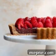 Dark chocolate raspberry tart on a white cake stand, topped with fresh raspberries and a glossy honey-jam glaze.