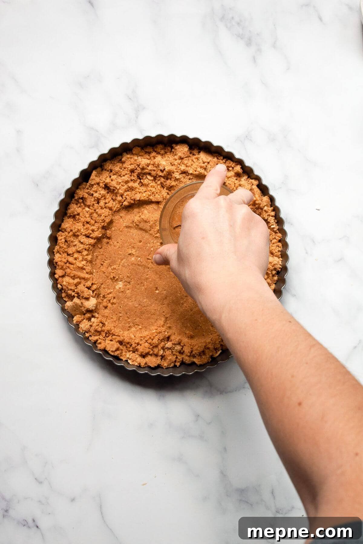 Dark Chocolate Raspberry Tart Recipe 5 Hand pressing graham cracker crust mixture into an 8-inch fluted tart pan.