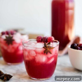 two cranberry margaritas sitting in front of a large pitcher of cranberry margaritas