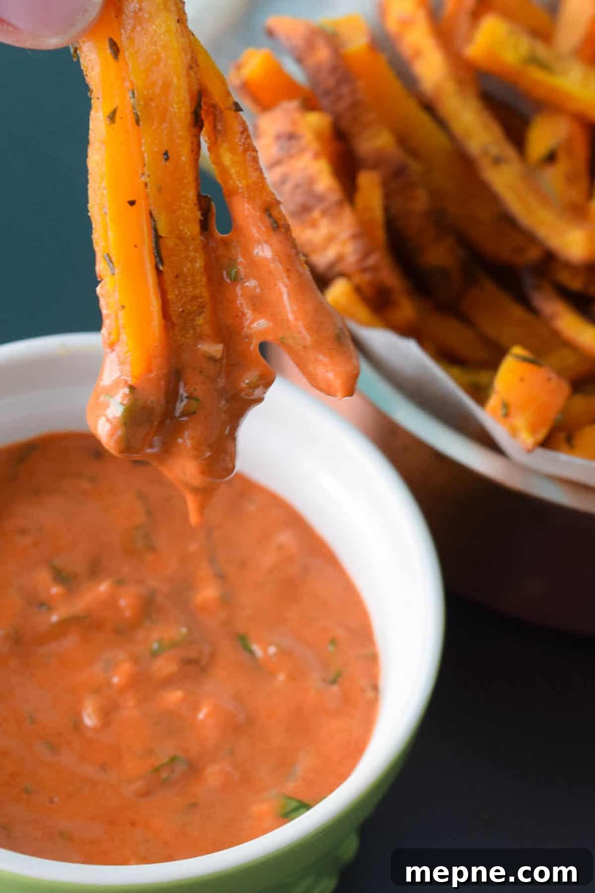 close up view of butternut squash fries being dipped into a red serving sauce
