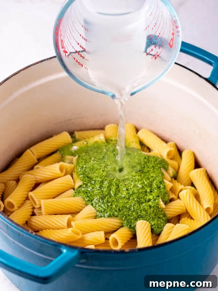 Pesto Rigatoni with Burst Cherry Tomatoes and Burrata 9 liquid measuring cup pouring starchy pasta water into a pot with cooked rigatoni and pesto