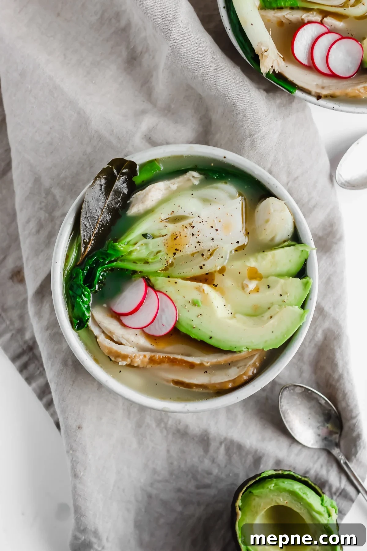 A bowl of asian-inspired leftover turkey soup next to a spoon.
