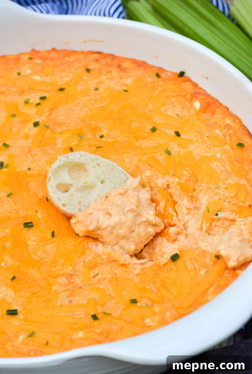a baguette slice dipped in a white bowl of creamy buffalo chicken dip