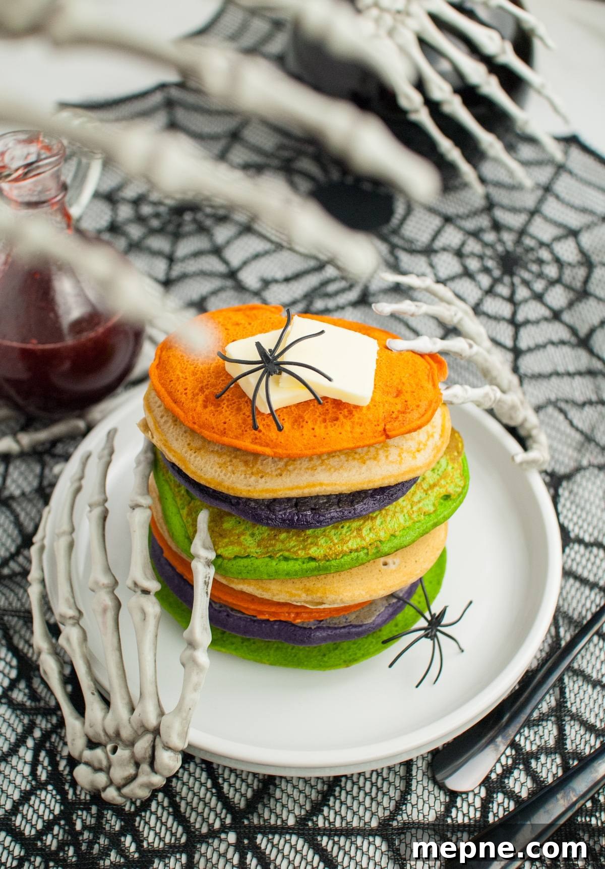 Colorful pancakes topped with butter and toy spiders, held by skeleton hands on a Halloween-themed table—spooky breakfast ideas perfect for Halloween recipes for kids.
