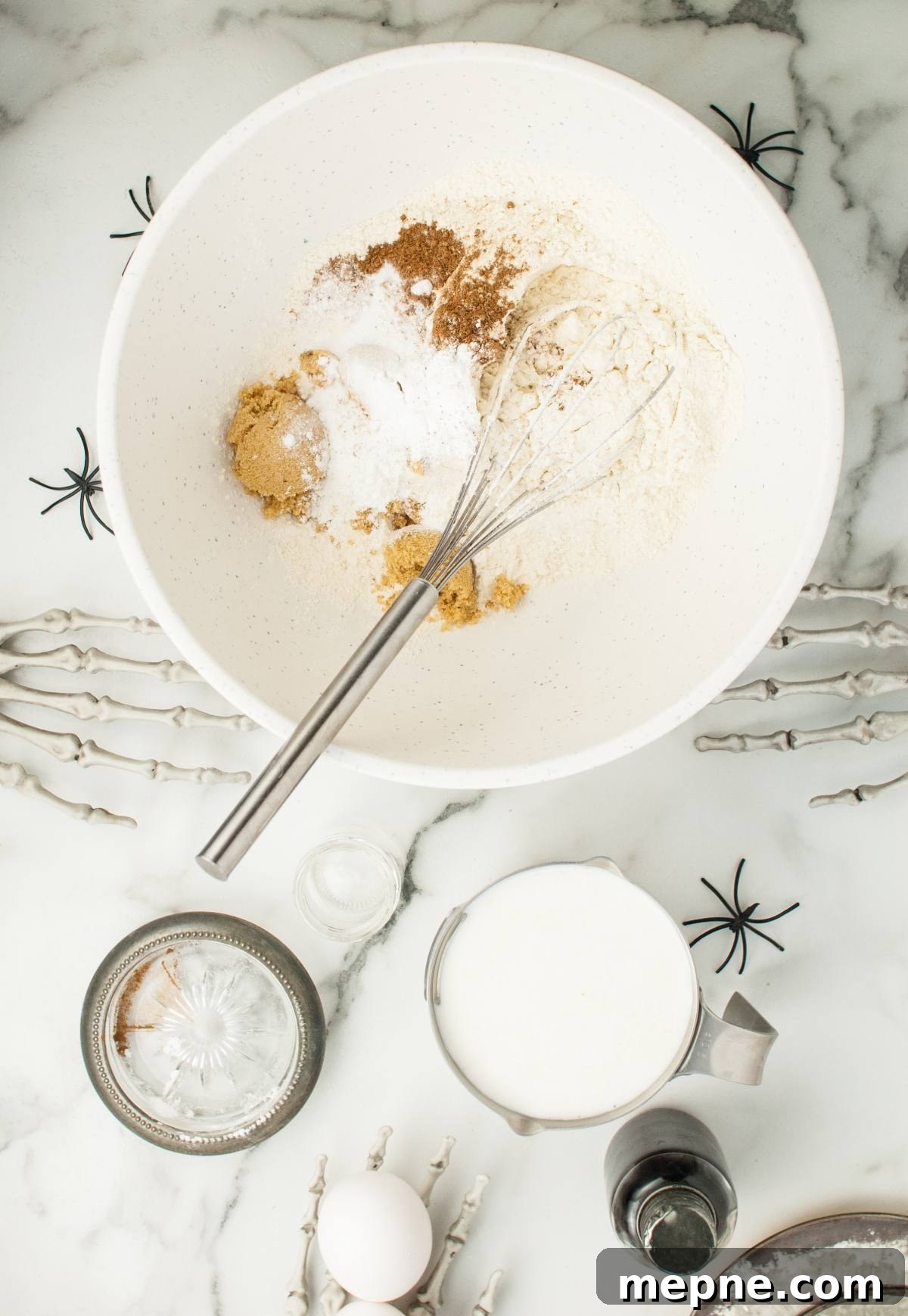 A mixing bowl with dry ingredients and a whisk, surrounded by Halloween skeleton hands and spiders—perfect for Halloween recipes for kids or creating spooky Halloween party food.