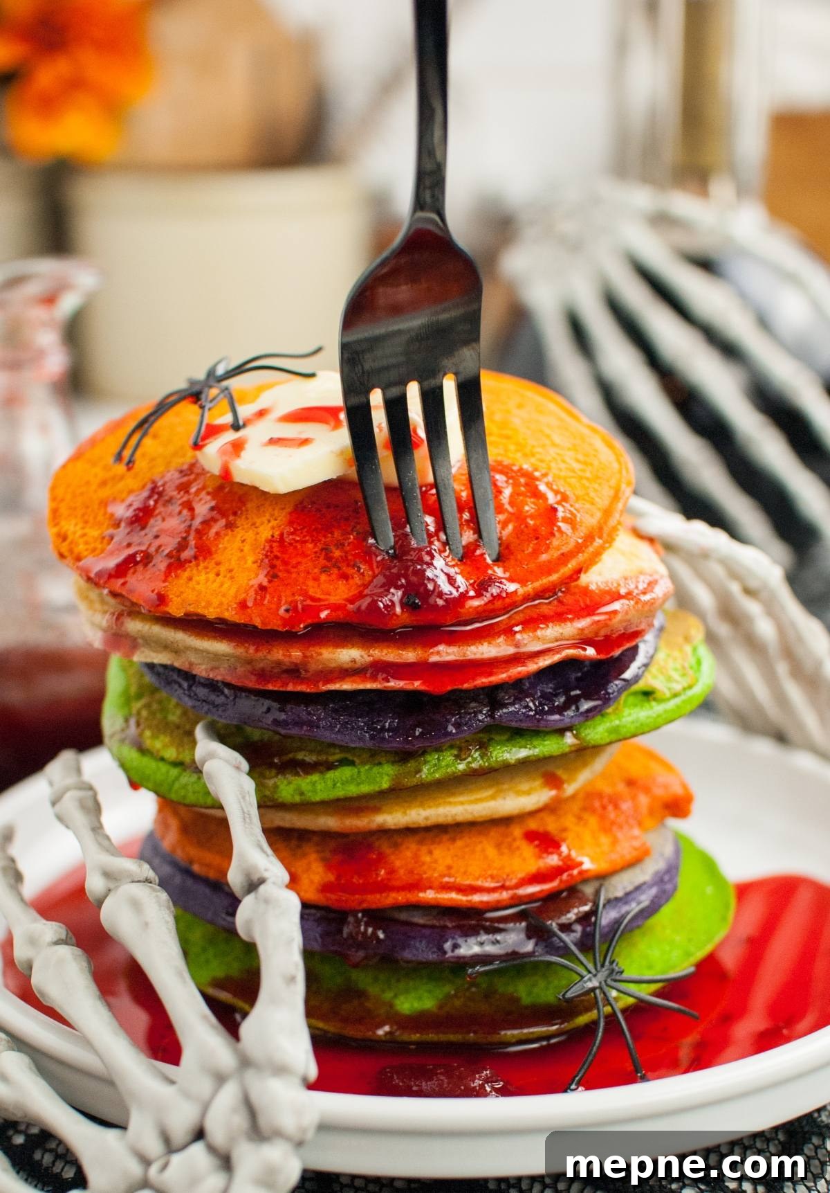 A stack of colorful pancakes with syrup, held by a skeleton hand and topped with fake spiders—perfect for spooky breakfast ideas or Halloween party food.