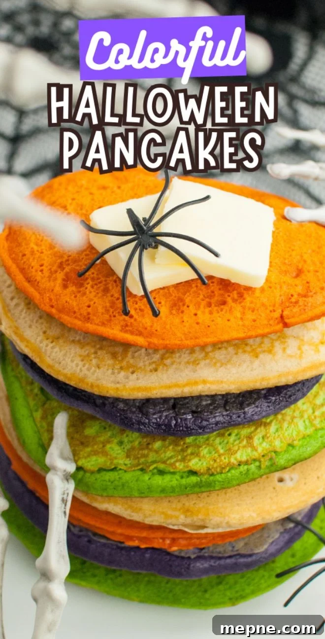 Stack of colorful Halloween pancakes—orange, green, and purple—with butter, a fake spider, and skeleton hands. Perfect Halloween party food to impress your guests! Fun idea if you want to learn how to make colourful pancakes.