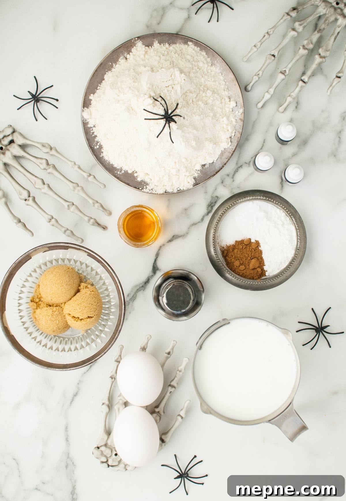 Baking ingredients on a marble counter with fake spiders and skeleton hands set the stage for spooky breakfast ideas and Halloween recipes for kids.