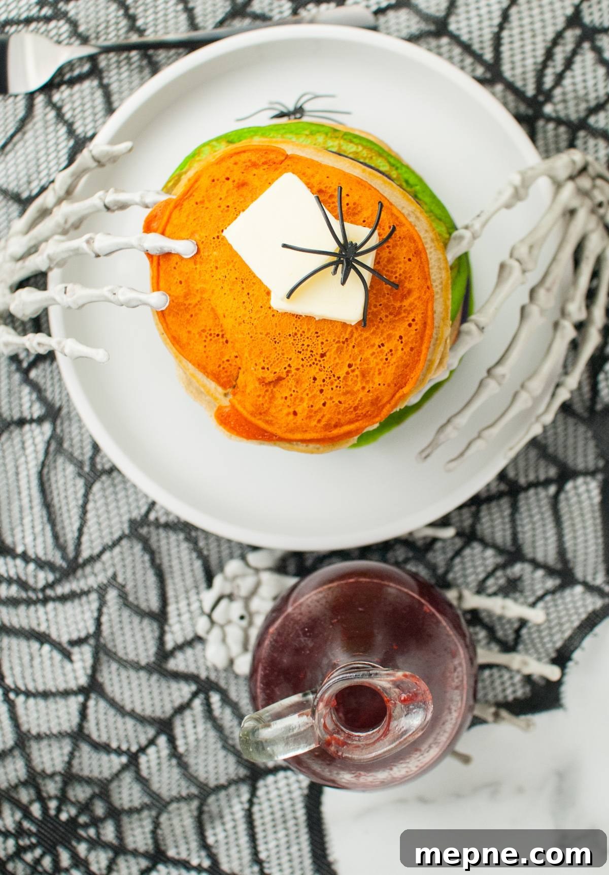 Stack of Halloween-themed pancakes with butter and fake spiders on a plate, held by skeleton hands—a fun addition to your Halloween party food and a great idea for Halloween recipes for kids.