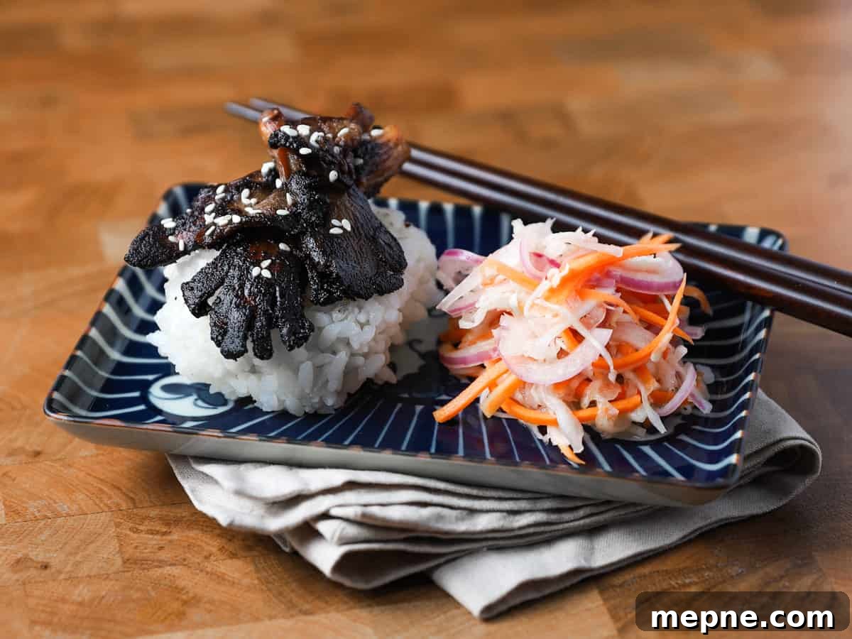 Crispy Chinese Fried Oyster Mushrooms with Vegan Char Siu Recipe 5 Photo of a dark blue patterned oblong dish resting on a napkin on a wooden table with Char Siu mushrooms, sushi rice and pickled salad.