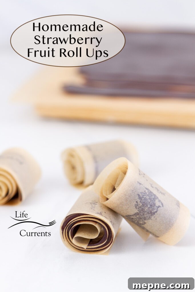 How to Make Strawberry Fruit Roll-Ups 2 strawberry fruit roll ups in parchment paper in front of a cutting board with the rest of the fruit smash on it