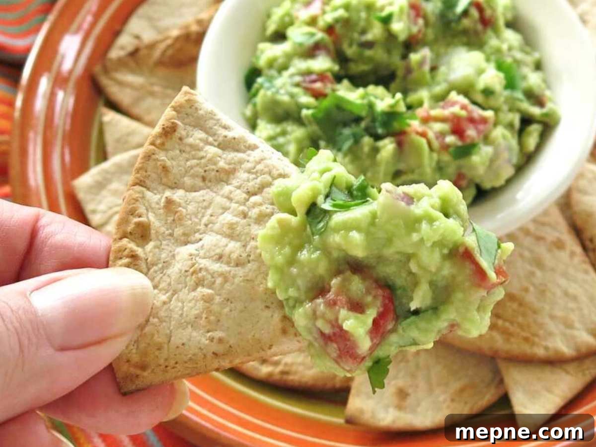 Over 15 Cinco de Mayo Dinner Recipes You'll Make Again 2 Fingers holding a tortilla chip with guacamole dip.