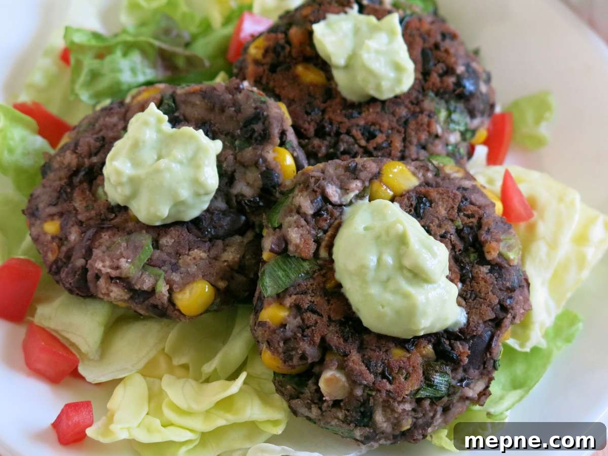 Three black bean cakes topped with avocado cream on a plate.