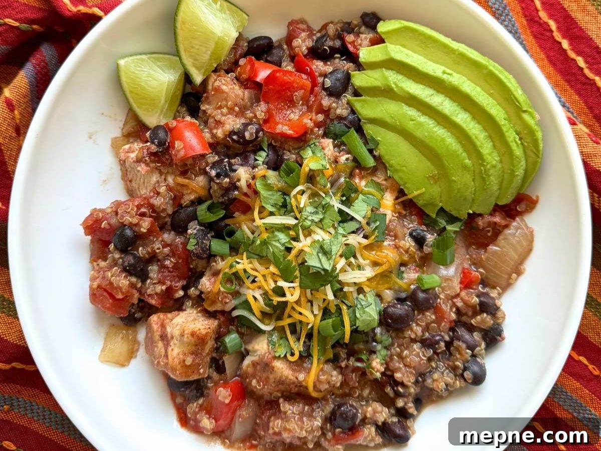White bowl with chicken and quinoa topped with sliced avocado, cheese, cilantro and lime wedges.