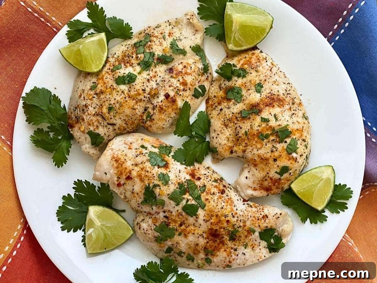Three baked chili lime chicken breasts on a white plate with lime wedges and cilantro.