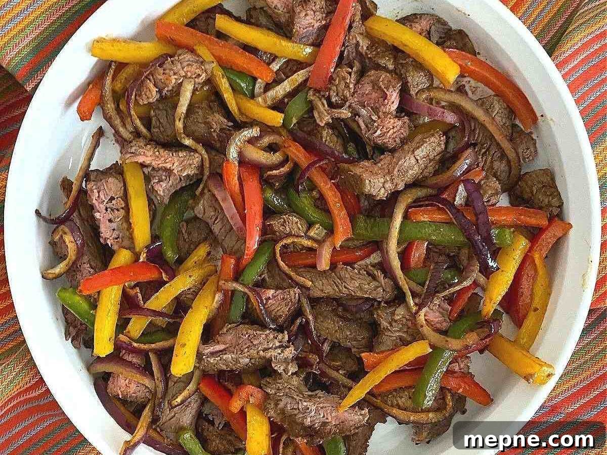 White platter with strips of steak, onion, and red, yellow, and green bell peppers.