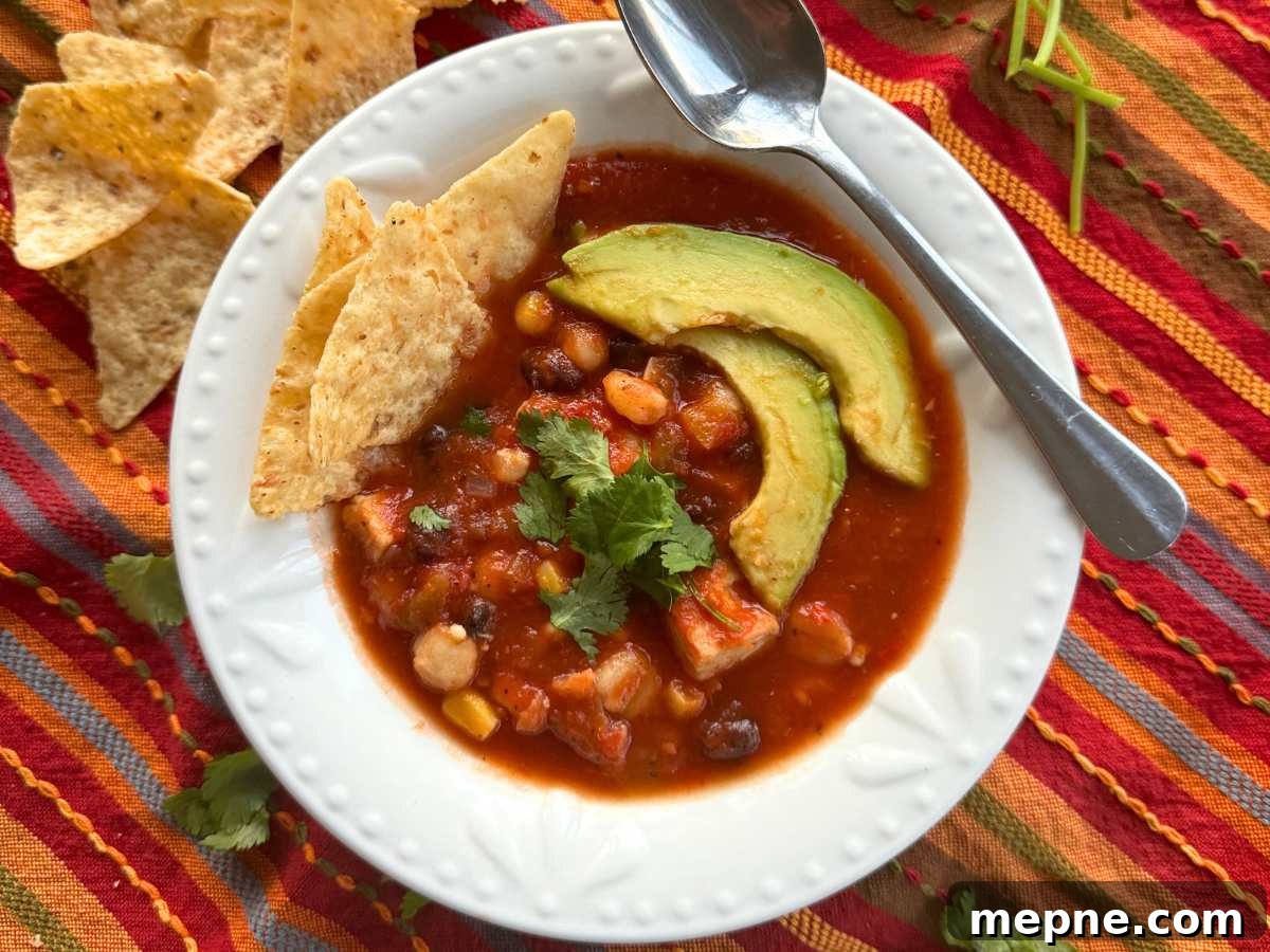 Chicken tortilla soup in a white bowl with a spoon topped with avocado slices and tortilla chips.
