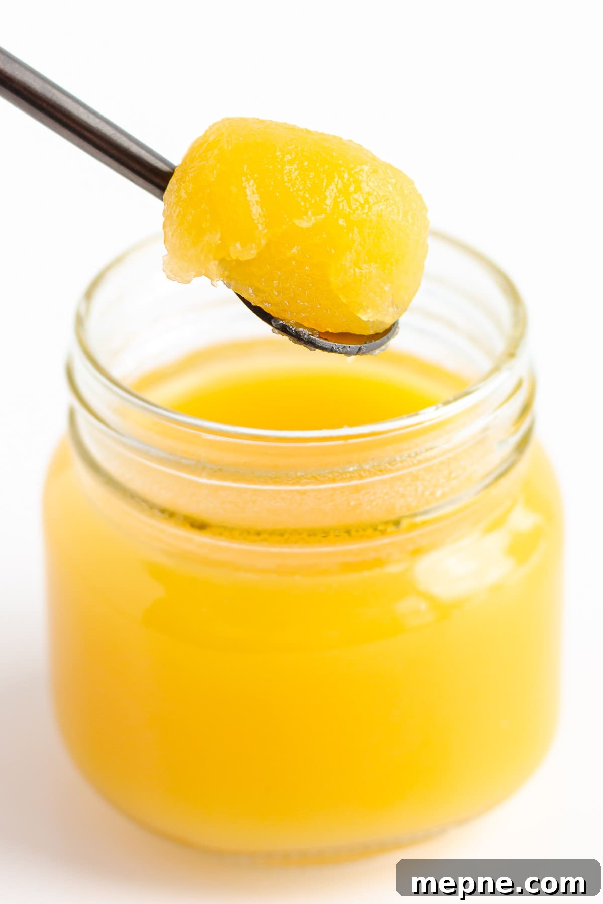 Homemade Mango Jelly Recipe with Fresh Mango 11 Fully set mango jelly being scooped out of small glass jar with a spoon.