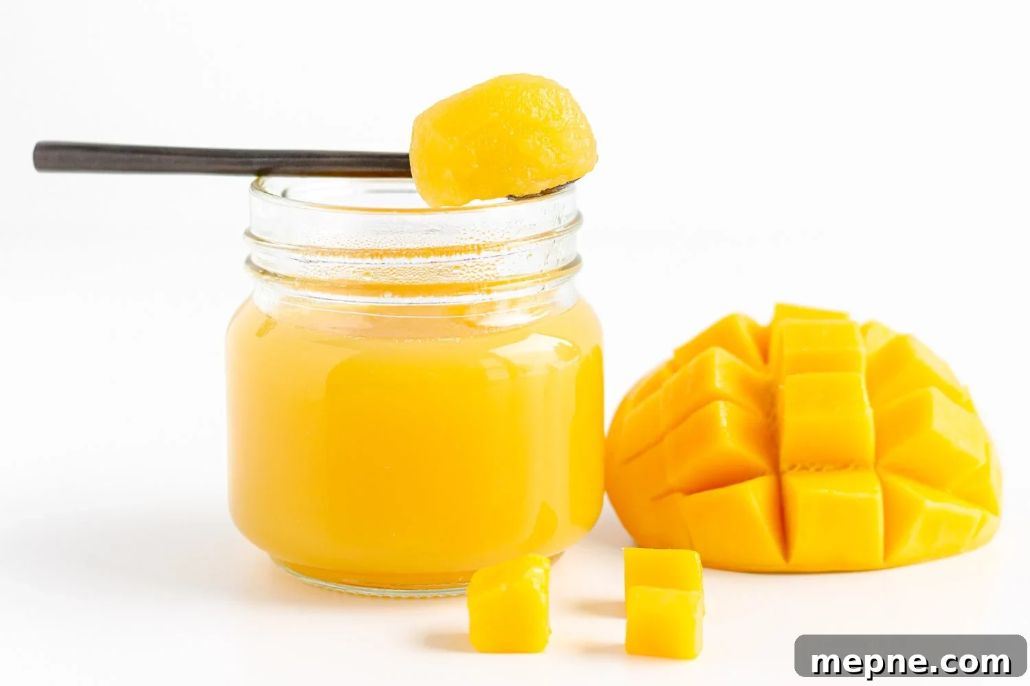 Homemade Mango Jelly Recipe with Fresh Mango 13 Mango jelly on a spoon set over a small glass jar filled with mango jelly beside some cut up fresh mango.