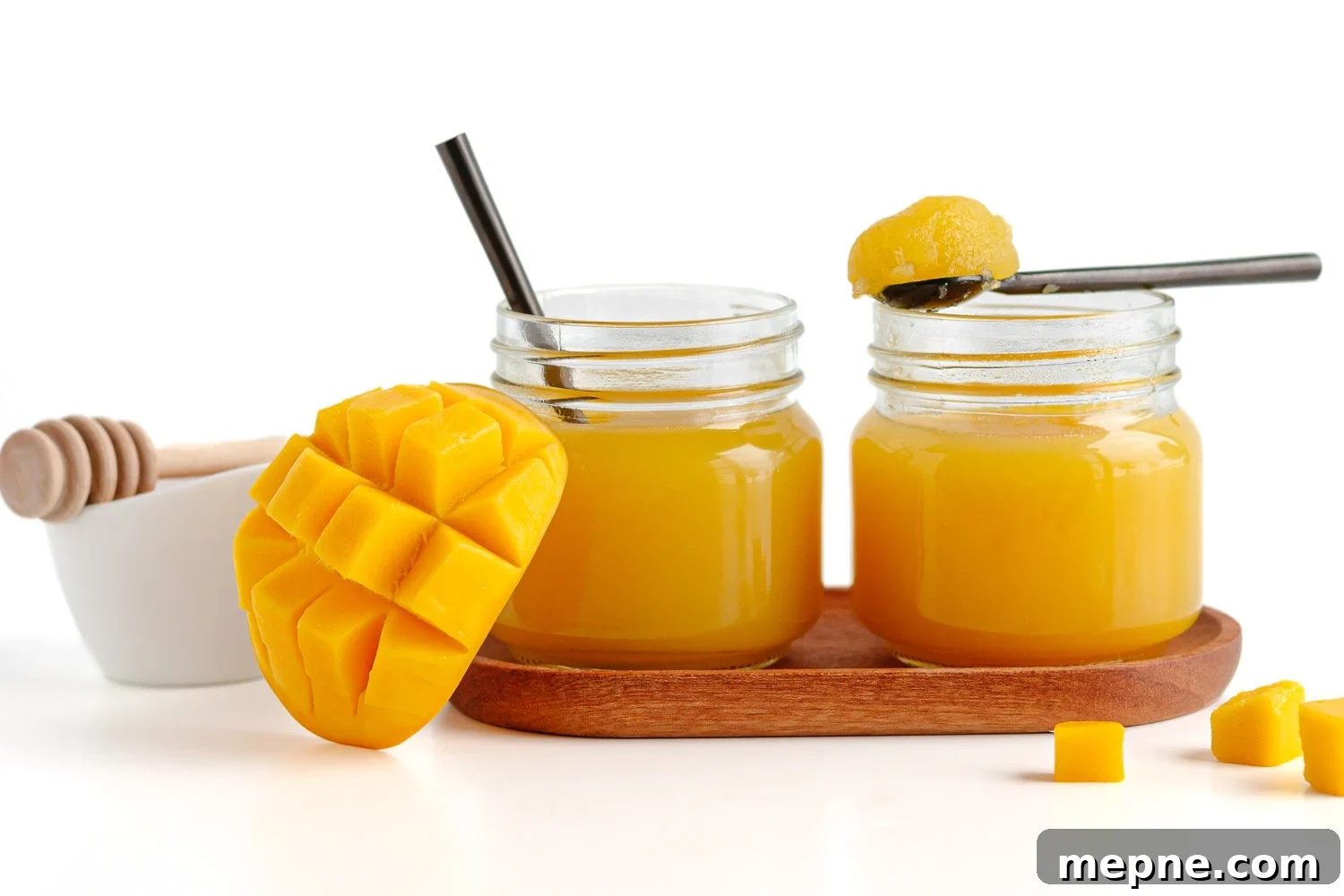 Homemade Mango Jelly Recipe with Fresh Mango 15 Homemade mango jello in 2 glass jars next to some sliced fresh mango and a small honey bowl.