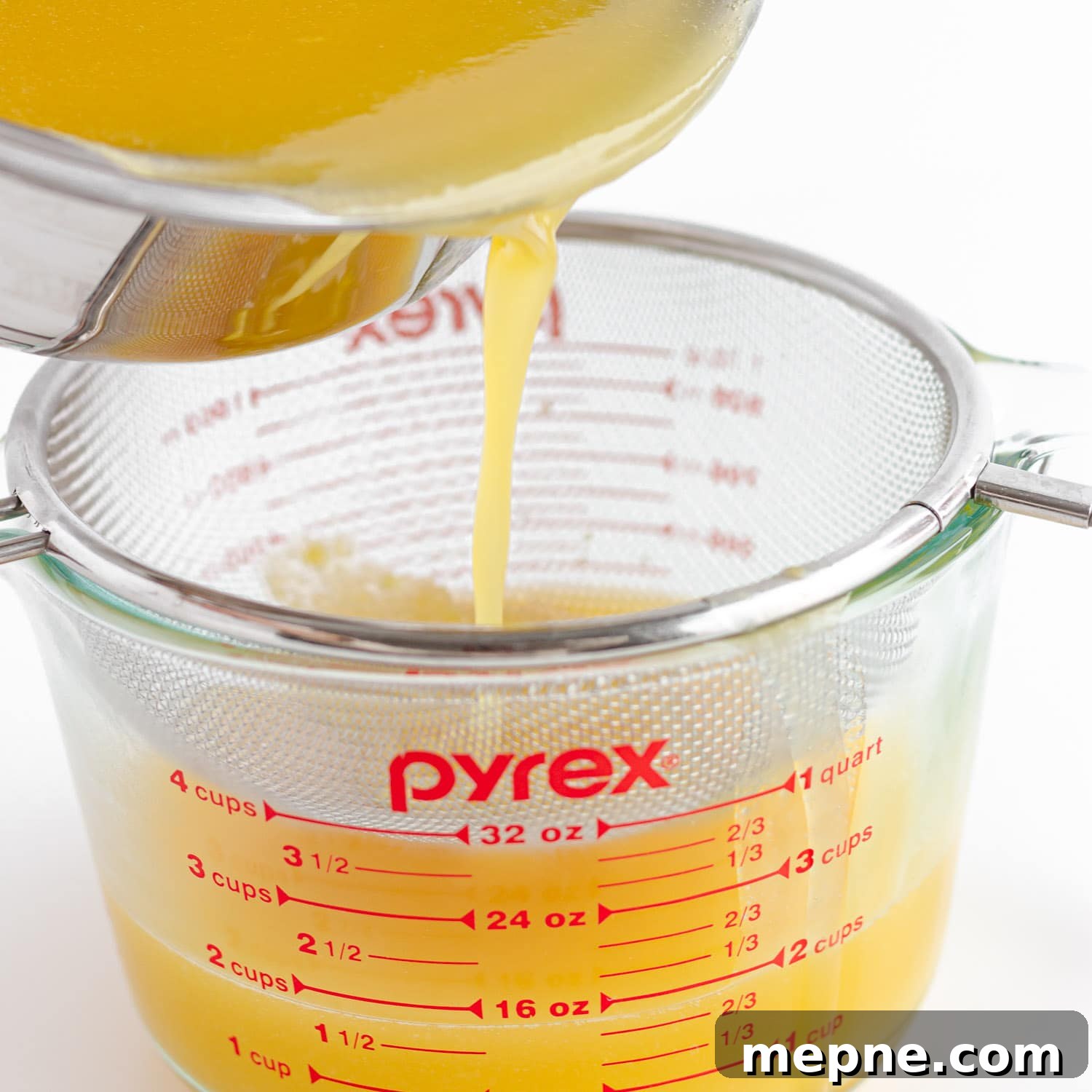 Homemade Mango Jelly Recipe with Fresh Mango 9 Pouring mango jelly mixture from the saucepan through a fine mesh sieve set over a large glass measuring cup.