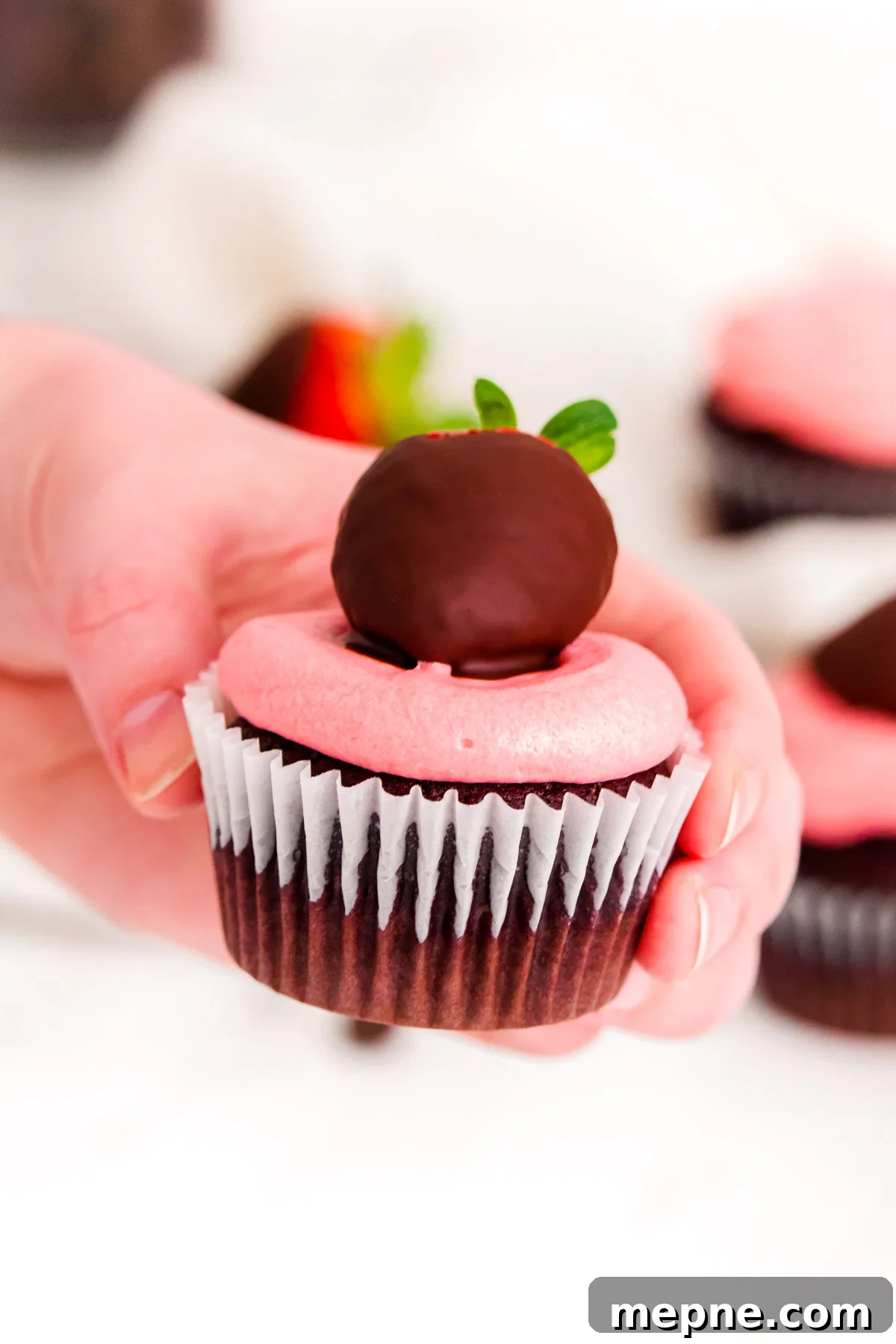 A woman's hand holding a chocolate covered strawberry cupcake.