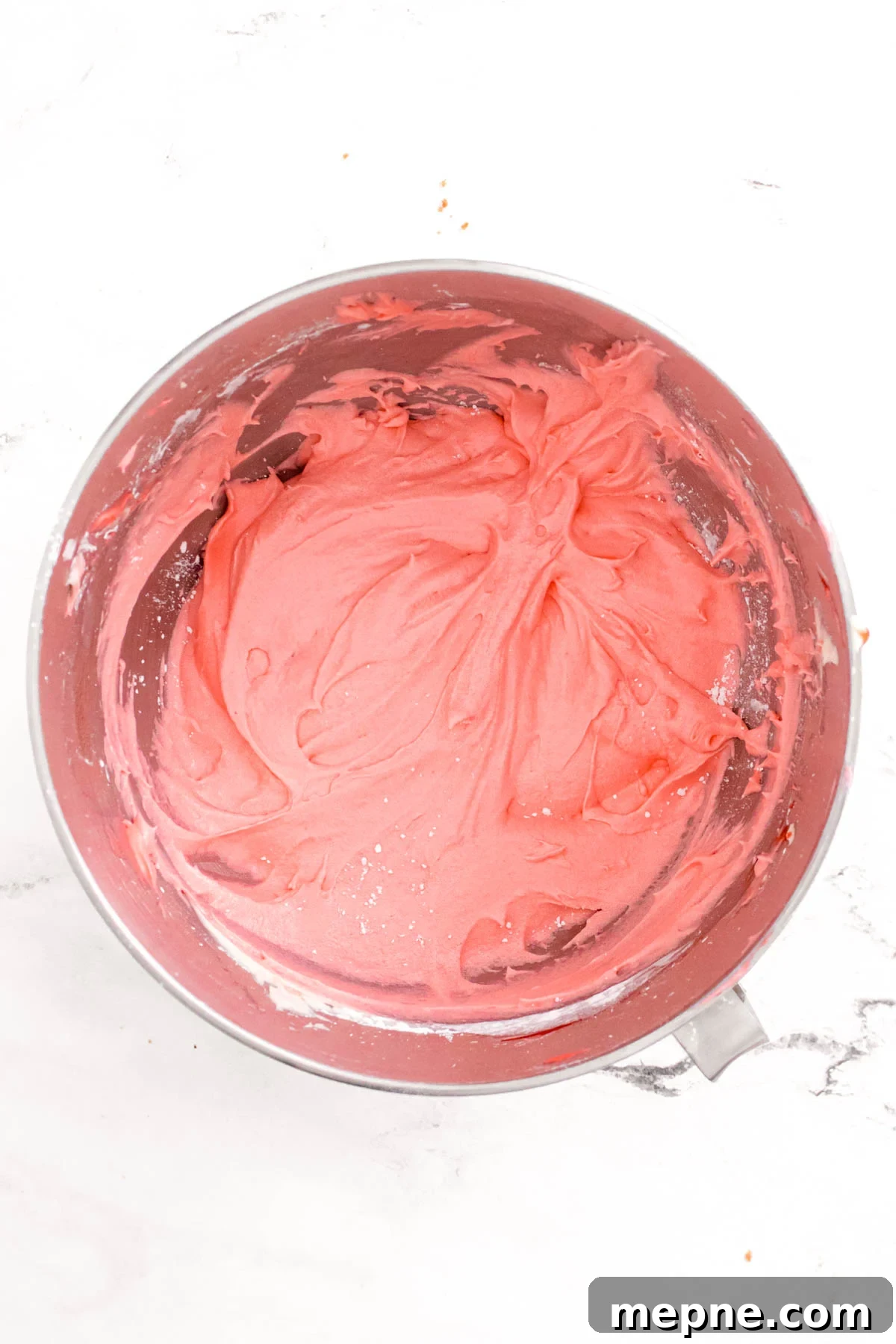 Overhead photo of strawberry frosting in a stainless steel mixing bowl.