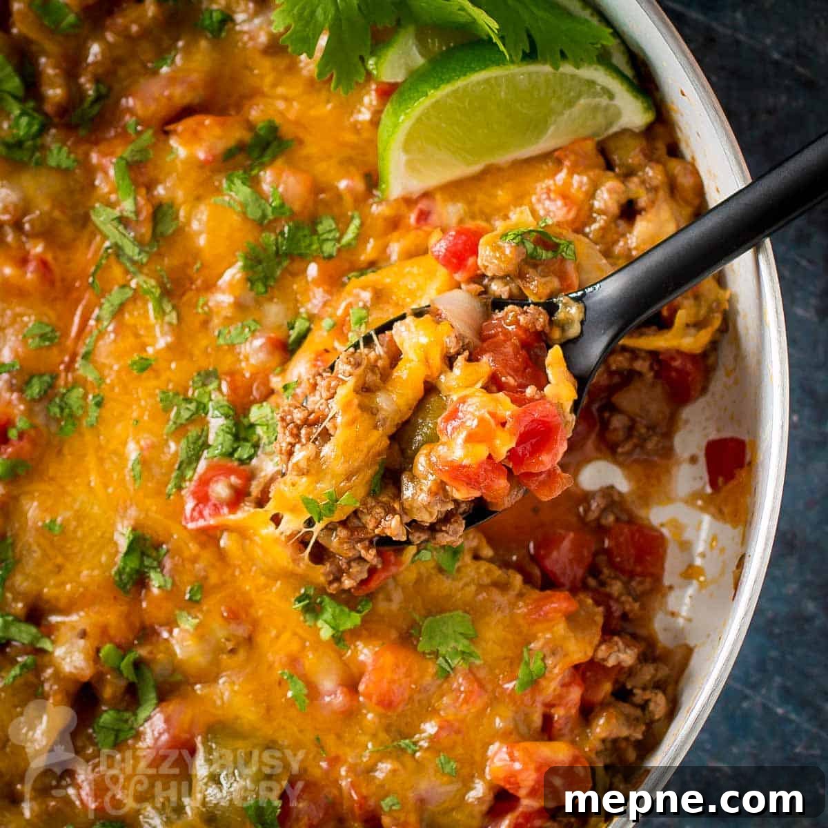 Affordable Meats to Buy and Cuts You Should Avoid 3 Overhead shot of cheesy taco filling garnished with fresh parsley and lime wedges being scooped out of a white skillet by a black spatula.