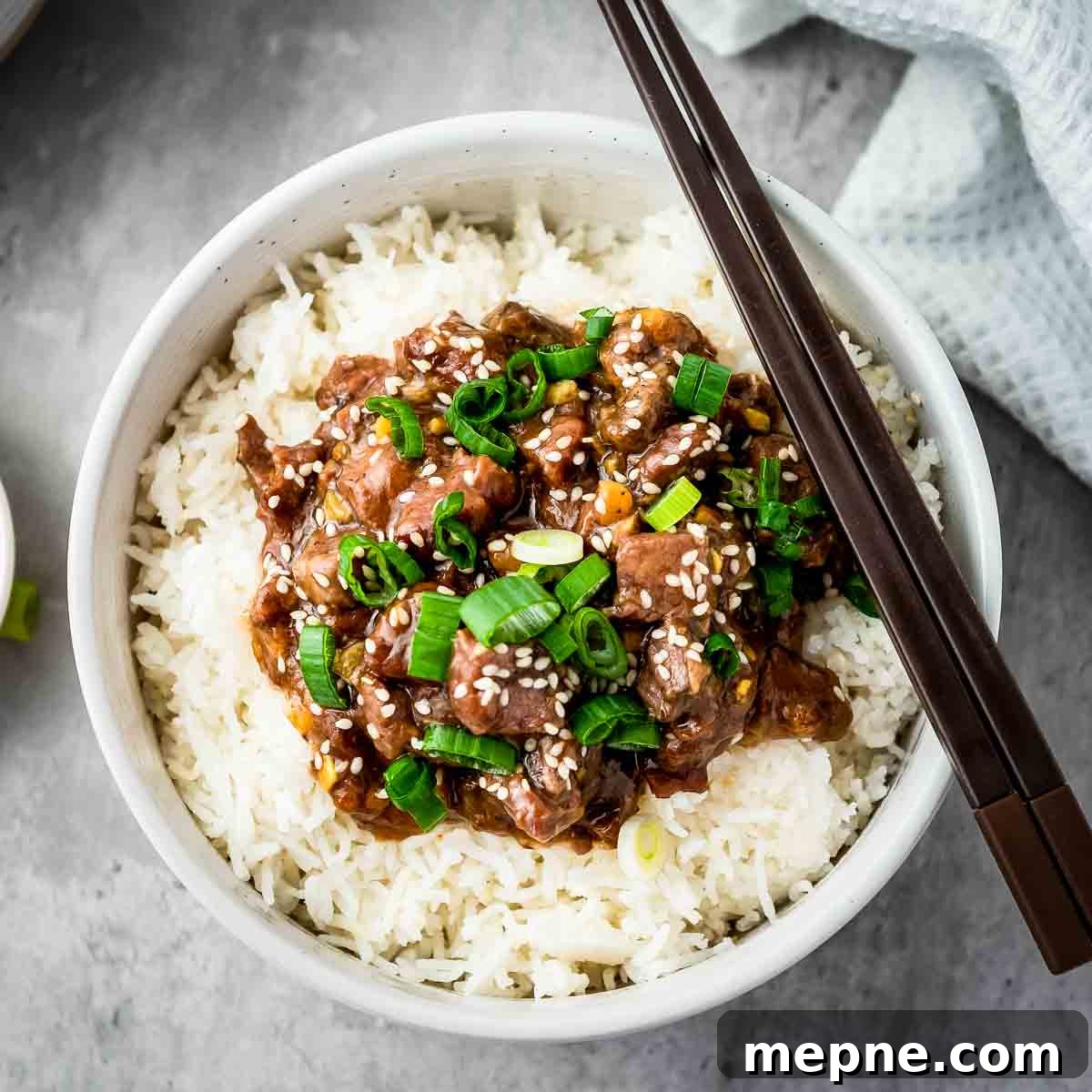 Affordable Meats to Buy and Cuts You Should Avoid 4 Overhead shot of mongolian beef over a bed of rice garnished with green onions in a white bowl with chopsticks on the side.