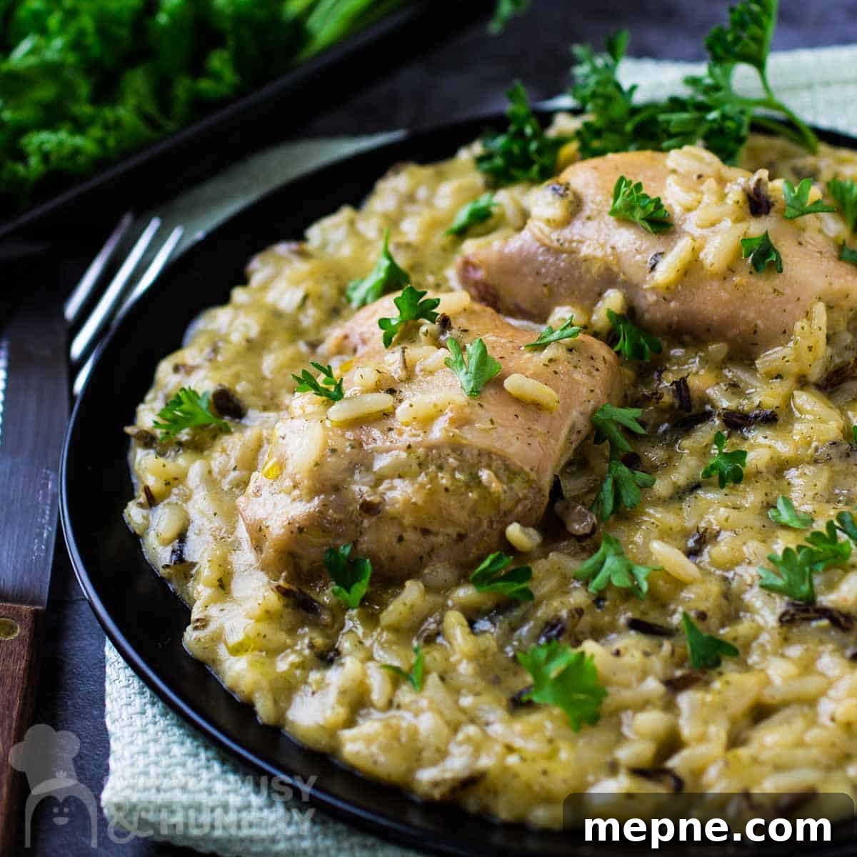 Affordable Meats to Buy and Cuts You Should Avoid 5 Side view of slow cooker chicken and wild rice on a black plate with a fork and knife on the side.