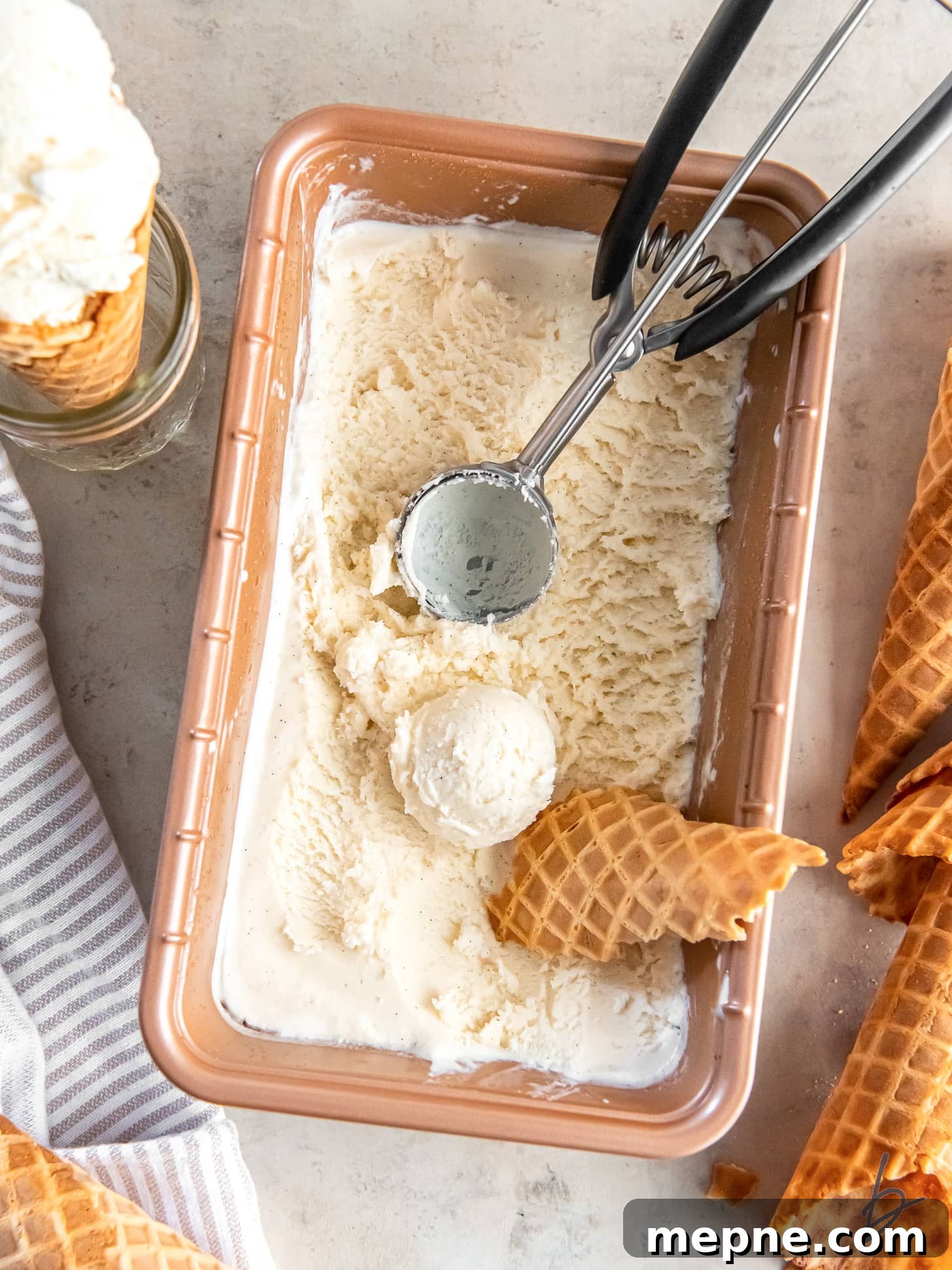 Creamy Eggless Vanilla Ice Cream Recipe 5 ice cream scooper in pan of ice cream with scoop next to piece of waffle cone.
