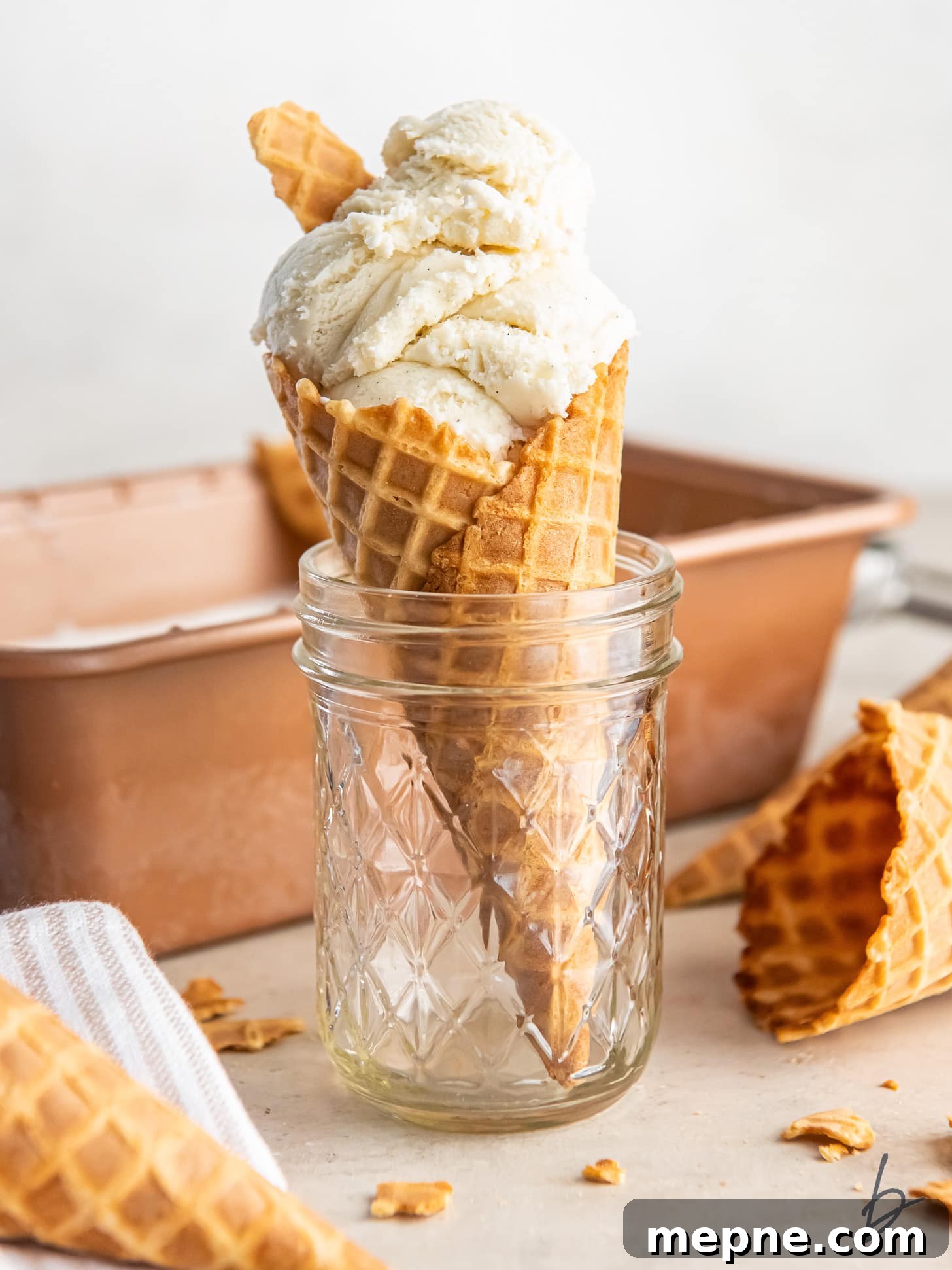 Creamy Eggless Vanilla Ice Cream Recipe 6 homemade vanilla ice cream in a waffle cone held up in a glass jar.