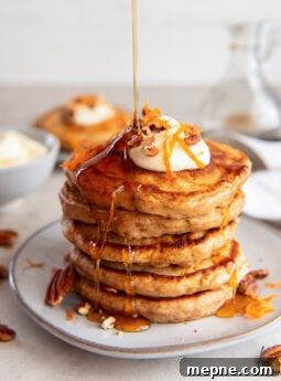 maple syrup poured on top and drizzling down a stack of carrot cake pancakes on a plate.
