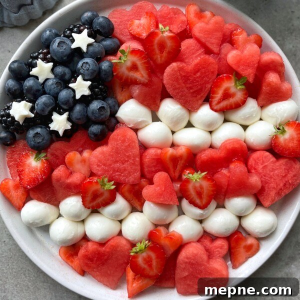 Red White and Blue Caprese Bites for Fourth of July 3 A patriotic plate arranged like the American flag with blueberries, blackberries, mozzarella balls, star-shaped cheese, sliced strawberries, and heart-shaped watermelon bites—perfect for festive food recipes or healthy party dishes.