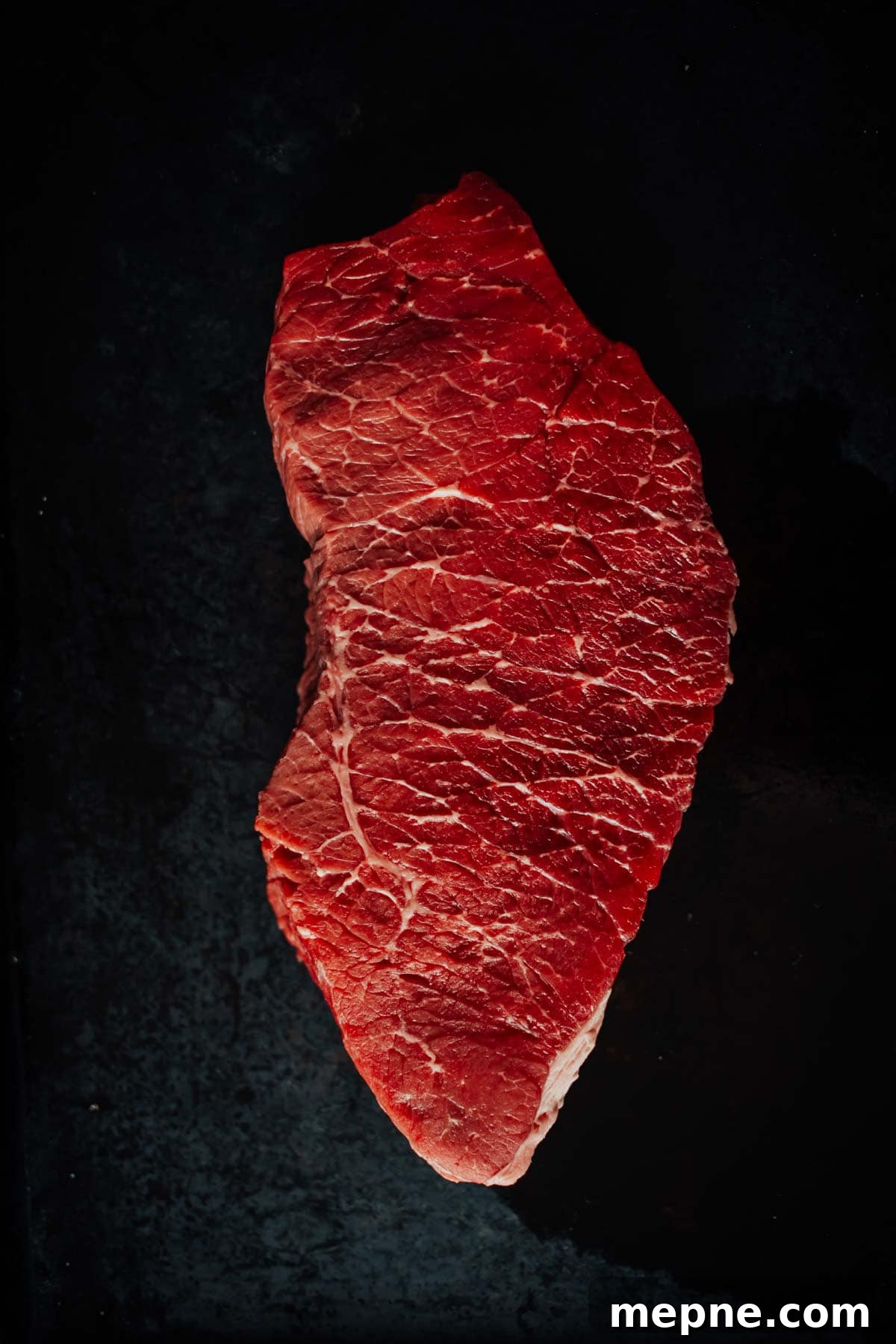 How to Grill London Broil for Tender Juicy Results 3 A raw, london broil steak against a dark background. The meat has a deep red color with visible marbling.
