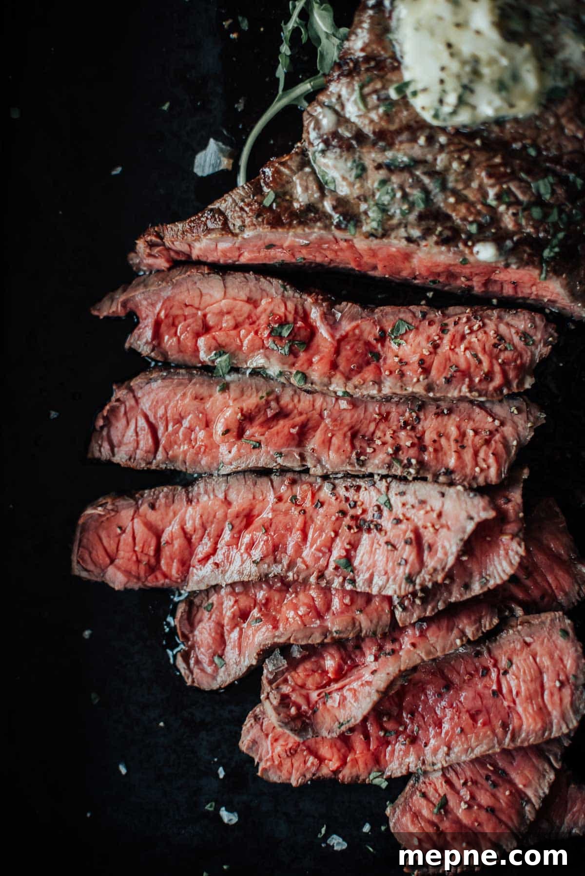 How to Grill London Broil for Tender Juicy Results 8 A sliced medium-rare london broil, garnished with herbs and served on a dark surface, with a dollop of melting butter on top.