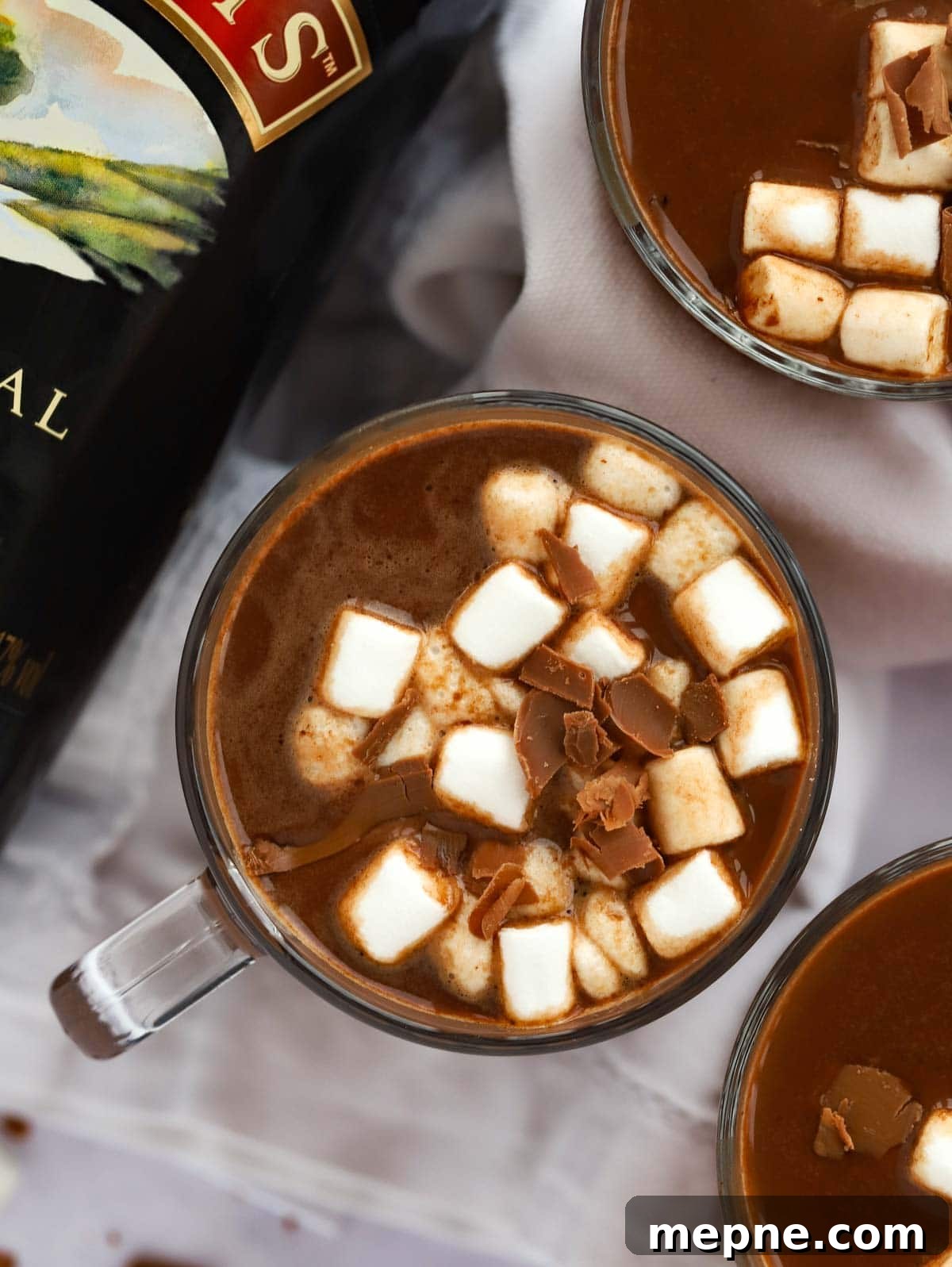 Slow Cooker Baileys Irish Cream Hot Chocolate Recipe 3 Festive Baileys Hot Chocolate in cups with marshmallows on top on a table.