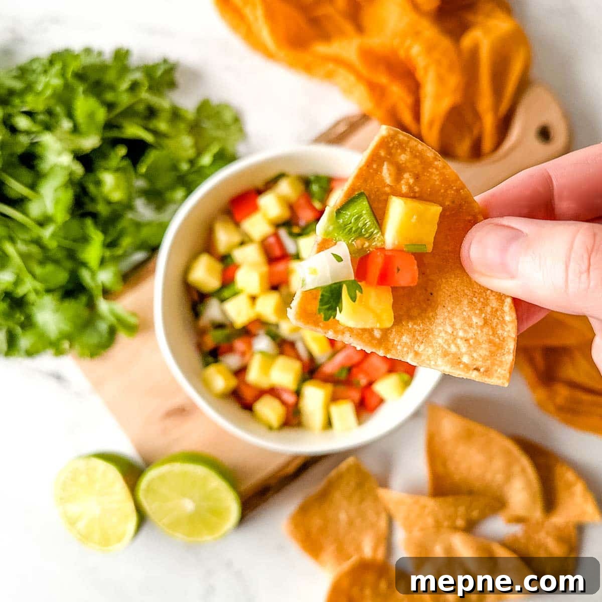 Pineapple Pico de Gallo Recipe: Tropical Salsa 12 Overhead shot of a chip with pineapple salsa on it over a bowl of pineapple pico de gallo in a white bowl.