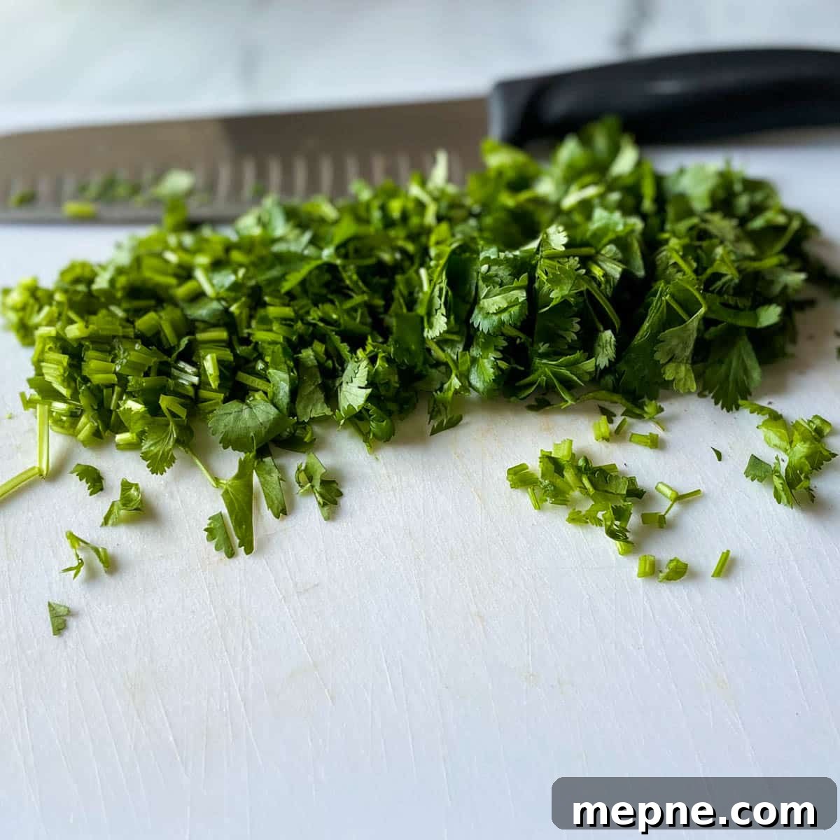 Pineapple Pico de Gallo Recipe: Tropical Salsa 7 Chopped fresh cilantro is shown on a white cutting board with a kitchen knife in the background.