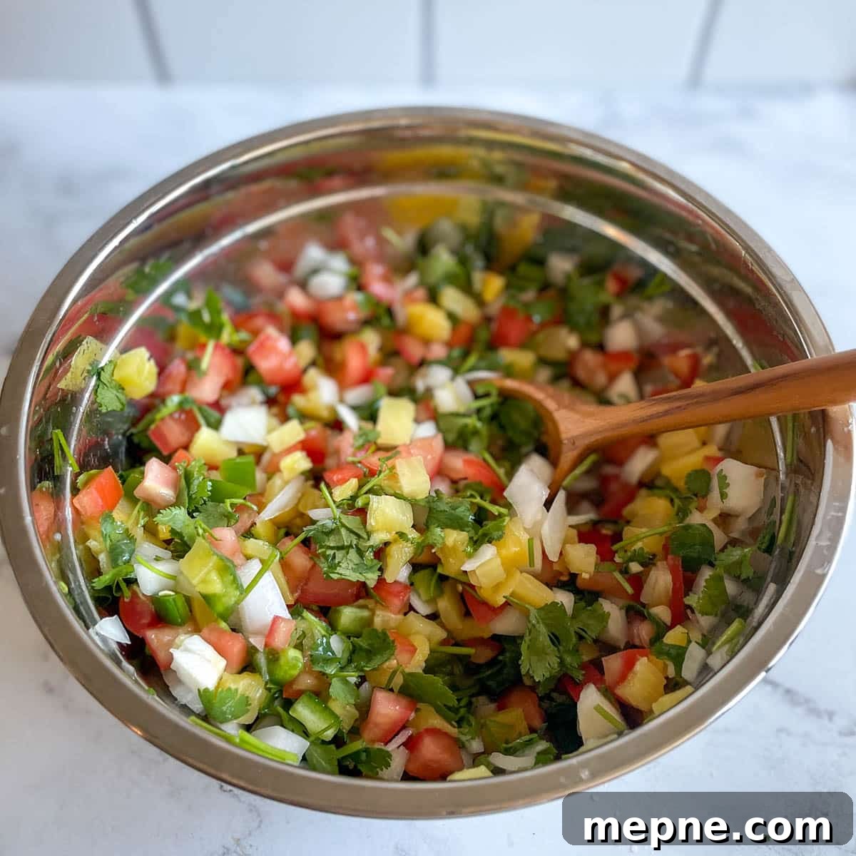 Pineapple Pico de Gallo Recipe: Tropical Salsa 10 Finished pineapple pico de gallo is shown in a stainless steel bowl with a wooden spoon.